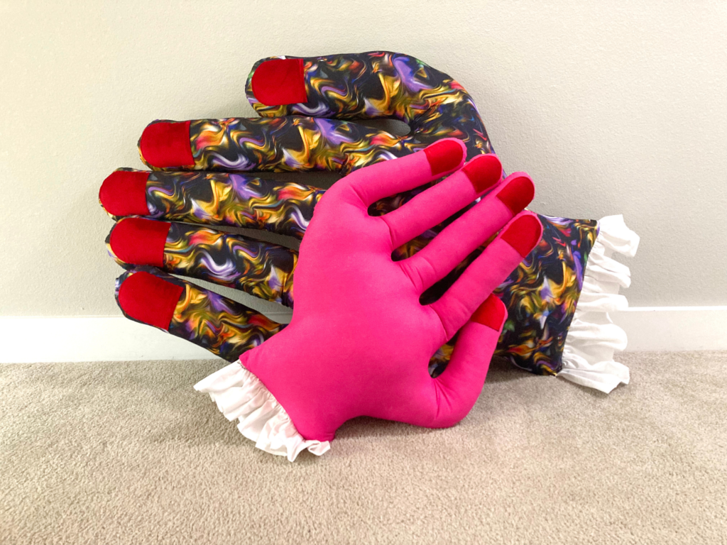 Pink mini hand pillow in front of a giant hand pillow in swirled print fabric