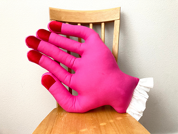Pink mini hand pillow with red fingertips on a wooden chair