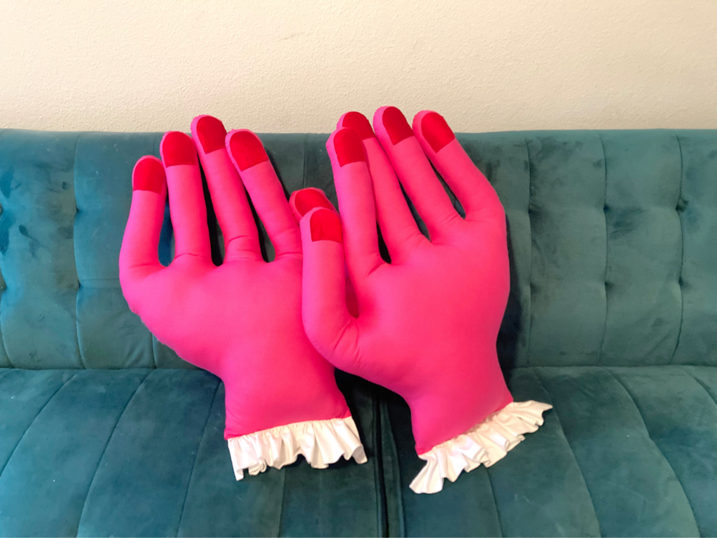 Two pink mini hand pillows with white ruffles on a teal couch